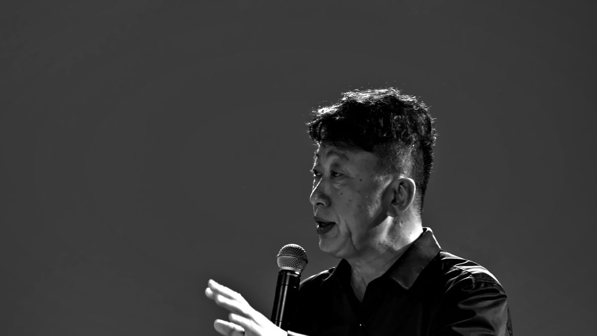 Weiping Ji speaks to the team with a microphone during a rehearsal